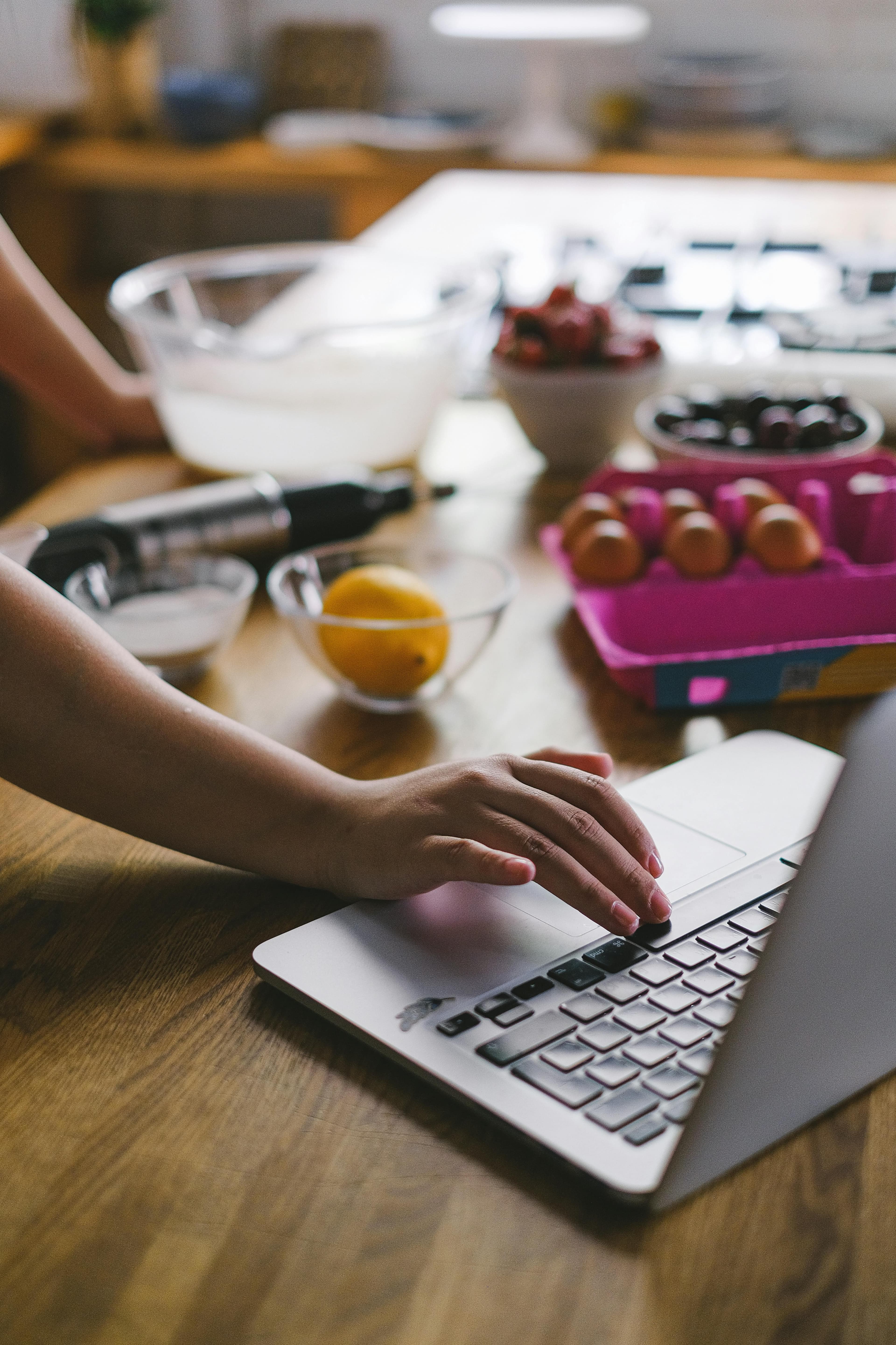 Using a laptop in the kitchen while ingredients are laid out for prep.